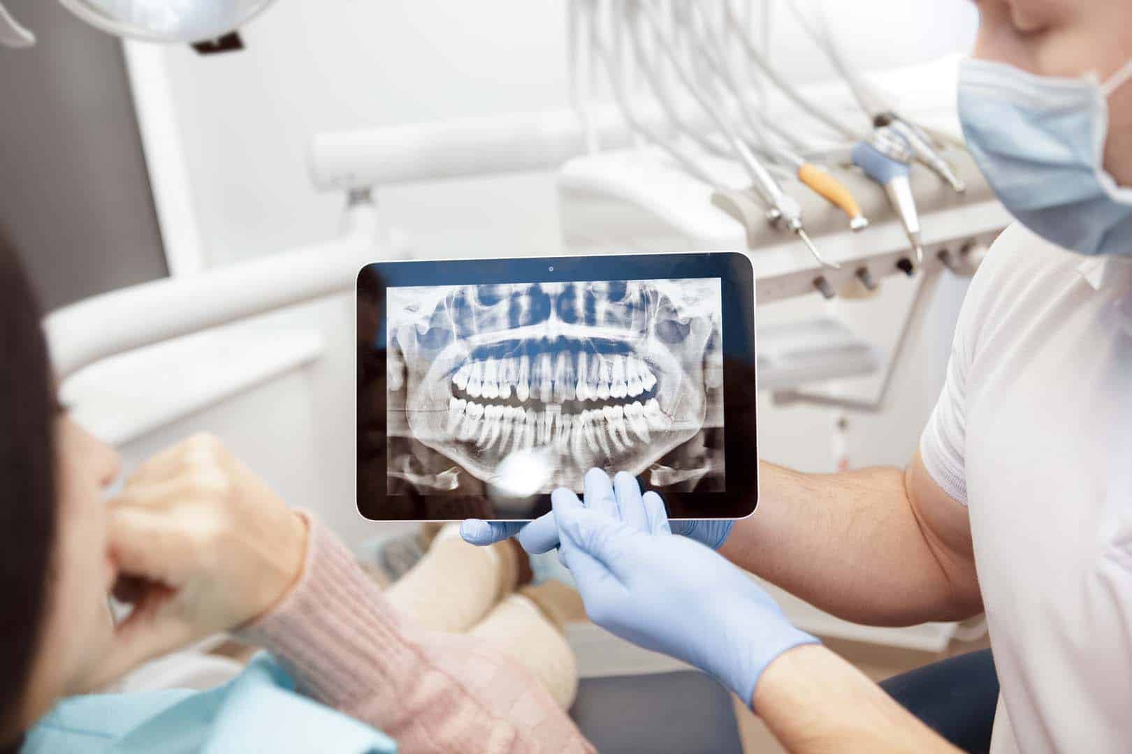 Professional dentist showing his client x rays on a digital tabl