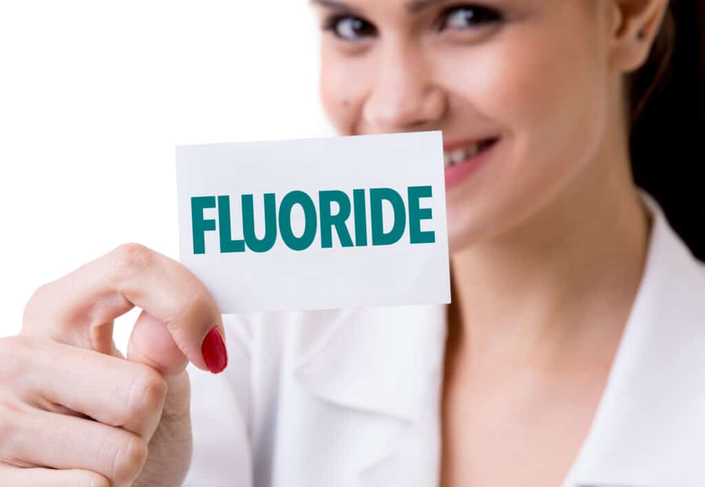 A dentist holding a card that says “Fluoride”